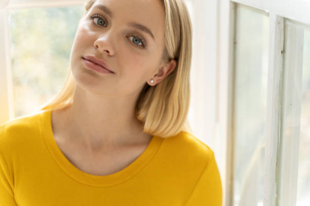 jeune belle fille dans le chandail jaune posant pour l'appareil-photo à la maison - women relaxation tranquil scene elegance photos et images de collection