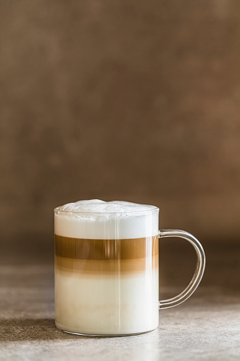 Caffe latte macchiato coffee on a brown gray table with beige background. Copy space room for text at the top.