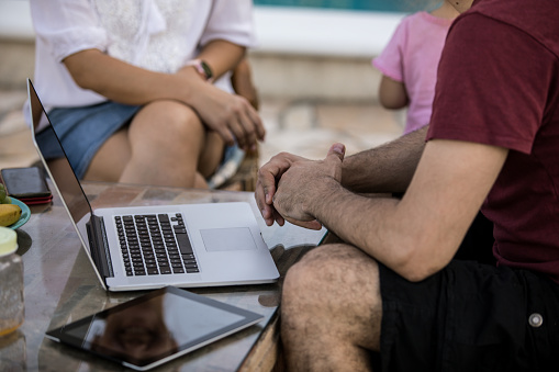 Midsection of unrecognizable couple sitting outdoors in their back yard and having fun and relaxing time together while the man is taking a break from using his digital tablet and laptop.