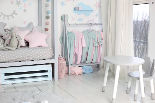 ropa para niños pequeños colgados en la habitación de los niños. estante con perchas con ropa de bebé. estante de tela para niños. color pastel niños ropa en una fila en open hanger interior. dormitorio de los niños.  decoración del hogar - parvulario dormitorio fotografías e imágenes de stock