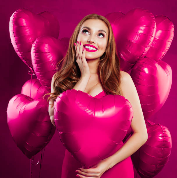 Pretty young woman with makeup and long ginger hair holding pink heart balloon on pink card backgroud Pretty young woman with makeup and long ginger hair holding pink heart balloon on pink card backgroud valentine s day holiday stock pictures, royalty-free photos & images