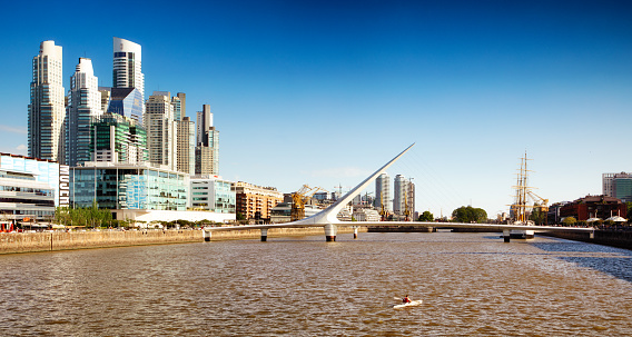 Panoramic view of Buenos Aires Puerto Madero canal with skyscrapers and the Puente de la Mujer bridge. Someboady is kayaking in the foreground.