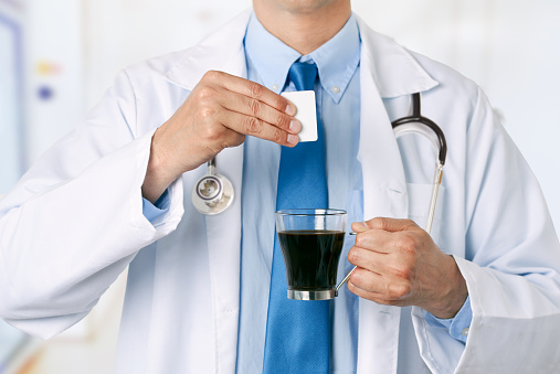 Cropped shot of a male doctor hands throwing saccharin into a coffee cup at hospital