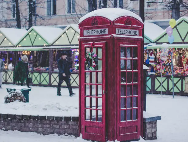 Photo of Christmas holidays concept of red classic English phone booth, season winter fair with people background in snowing weather