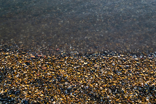Horizontal background of pebbles on a beach. A half of pebbles are under water. Top view.