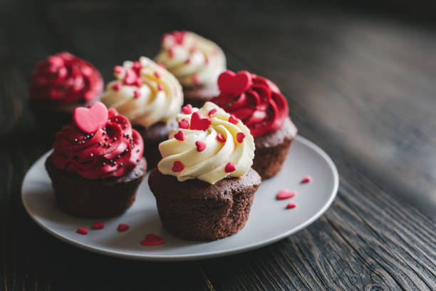 Valentine cupcakes in red color, served on the plate and decorated with sweet hearts. Valentine cupcakes in red color, served on the plate and decorated with sweet hearts. Dark wooden table. Selective focus. heart shape valentines day chocolate candy food stock pictures, royalty-free photos & images