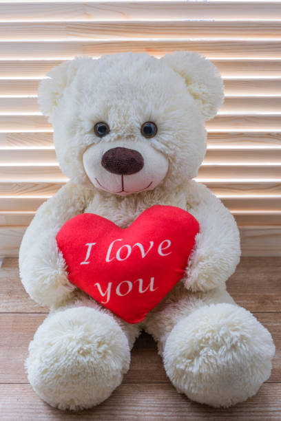 Cute Teddy Beige Bear Sits On A Background Of Wooden Blinds He Holds A Big  Red Heart With The Text I Love You Stock Photo - Download Image Now - iStock