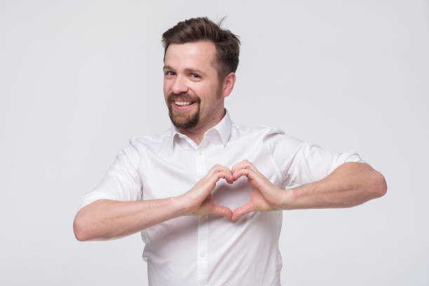 istock Friendly man with beard smiling and showing heart shaped hands gesture 1200167517