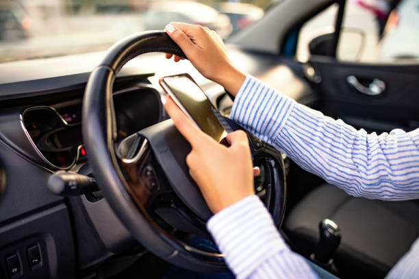 istock Young woman looking to her smartphone while driving car 1200172221