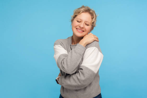 love yourself. cute happy woman with short curly hair in sweatshirt embracing herself and smiling with pleasure - urgency body care young adult people imagens e fotografias de stock