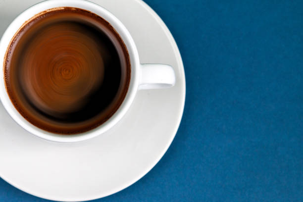 Black coffee espresso in a cup and saucer, blue  color background with empty space for text, unhealthy food concept
