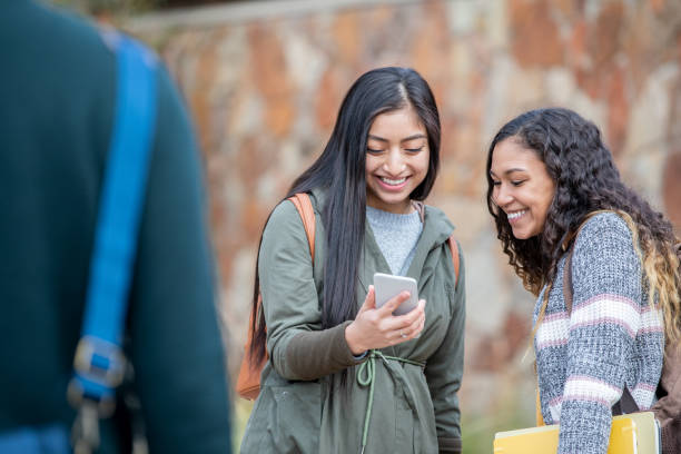 istock College student friends smile and look at mobile phone while walking outdoors between classes 1200188723