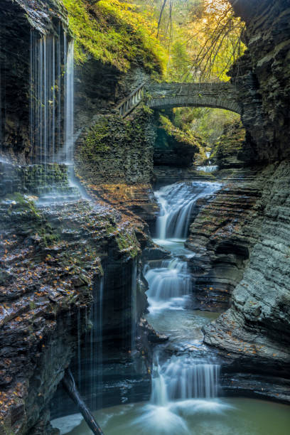 Rainbow Bridge and Falls in Autumn Rainbow Bridge  crosses above many-layered Rainbow Falls in Watkins Glen State Park, New Y0rk watkins glen stock pictures, royalty-free photos & images