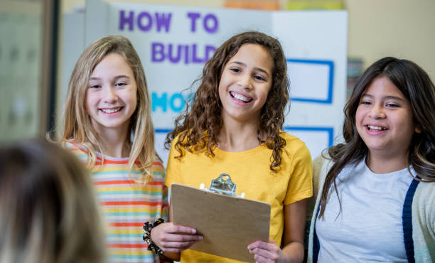 Two cheerful students, a boy and a girl with diverse backgrounds, give thumbs up in a school science lab, surrounded by educational tools and equipment.