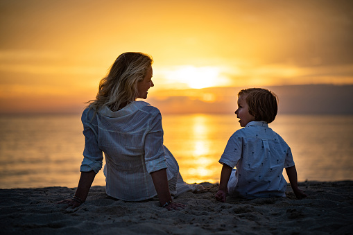 Rear view women and small boy sitting at the beach on sunset