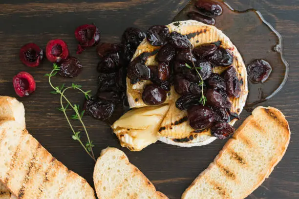 Grilled brie cheese topped with thyme-infused honey and sweet cherries, served with grilled ciabatta slices