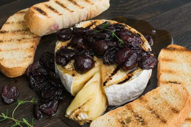 Grilled brie cheese topped with thyme-infused honey and sweet cherries, served with grilled ciabatta slices