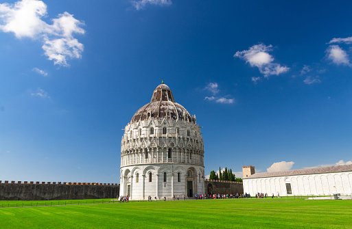Pisa Baptistery Battistero di Pisa on Piazza del Miracoli Duomo square green grass lawn, city wall, Camposanto cemetery, blue sky with white clouds copy space background in sunny day, Tuscany, Italy