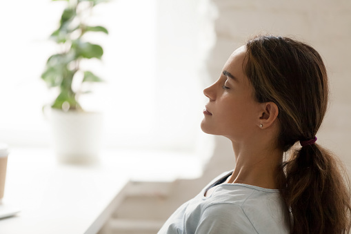 Side view young mixed race woman relaxing with closed eyes at workplace. Peaceful biracial lady freelancer deeply meditating, doing breathing exercises, enjoying break time, reducing stress at office.