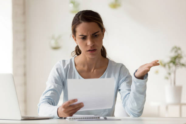 Stressed millennial mixed race woman reading paper with bad news. Head shot portrait stressed millennial mixed race woman reading paper with bad news. Frowning female employee irritated by dismissal notice. Unhappy young lady disagree with false information. unfairness photos stock pictures, royalty-free photos & images
