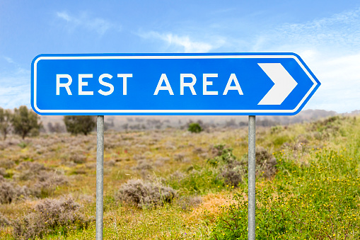 Blue rest area sign on side of road with blue sky and green vegetation