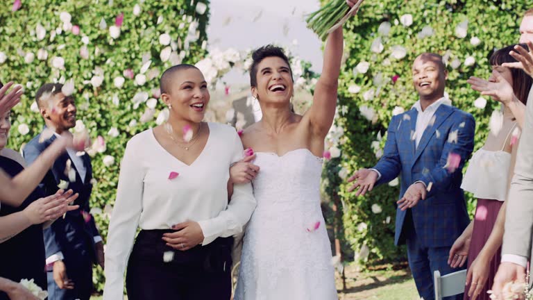 4k video footage of an affectionate young lesbian couple leaving their wedding venue with their guests throwing confetti on them