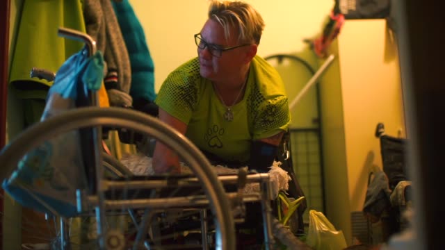 A disabled woman is transferred to a wheelchair in the corridor her apartment.