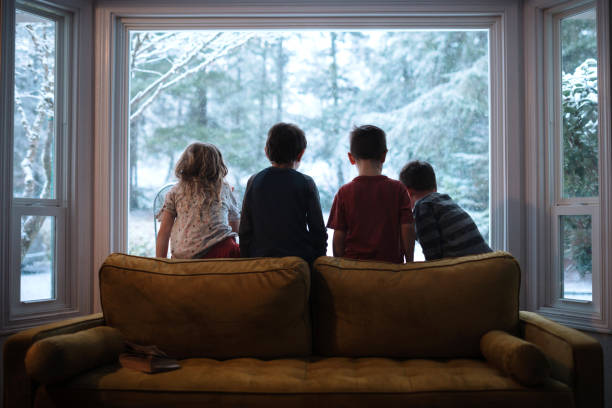 kinder, die bei fallendem schnee aus dem fenster schauen - winter family child snow stock-fotos und bilder