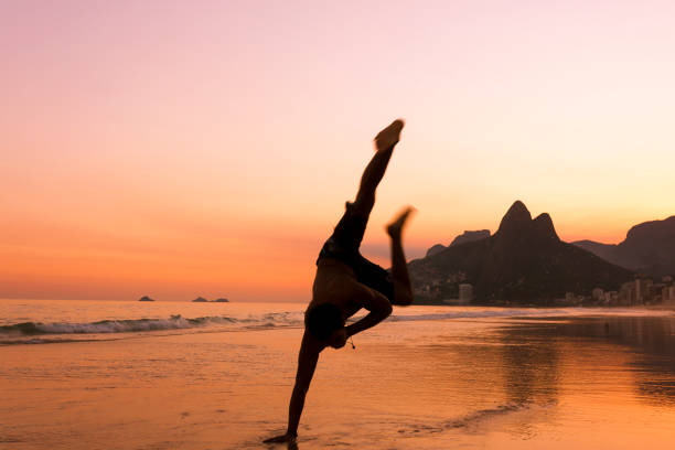 one hand stand, capoeira acrobatic yoga pose en una hermosa puesta de sol en la playa de ipanema en río de janeiro, brasil - brazil beach copacabana beach recreational pursuit fotografías e imágenes de stock