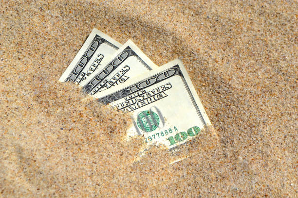 istock Money dolars half covered with sand lie on beach close-up 1200265446