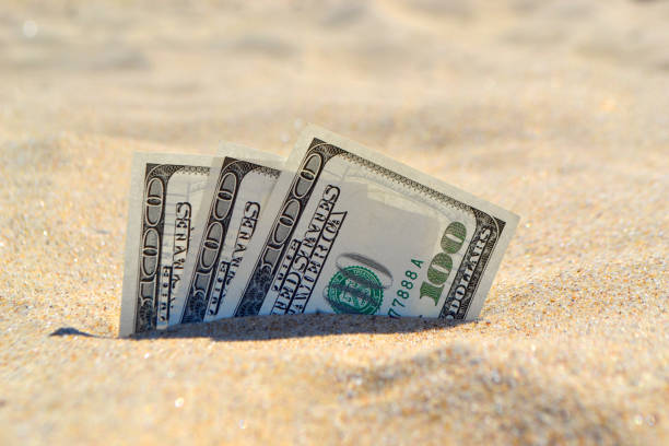 istock Money dolars half covered with sand lie on beach close-up 1200265452