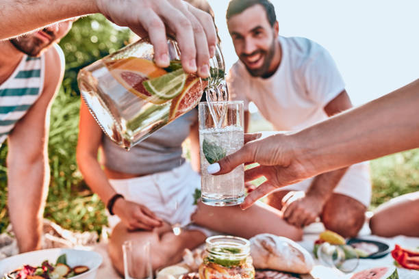 Guy pouring fresh homemade lemonade into glass of his girlfriend at outdoor party Guy pouring fresh homemade lemonade into glass of his girlfriend at outdoor party. People background. Close up view. Selective focus jug photos stock pictures, royalty-free photos & images