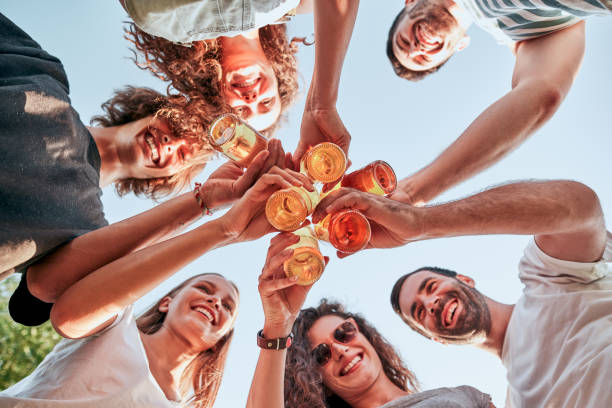 imagen de vista abajo de un grupo de amigos felices que clan botellas de cerveza de pie juntos - clunking fotografías e imágenes de stock