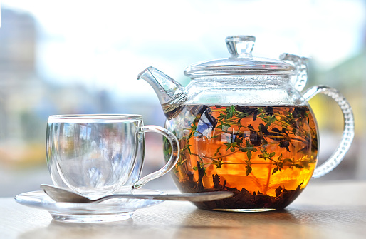 GLASS KETTLE WITH TEA AND EMPTY GLASS CUP ON A LIGHT BACKGROUND