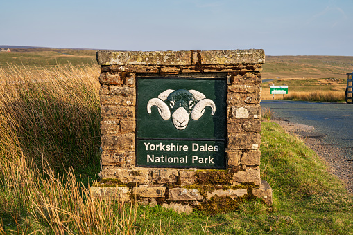 Near West Stonesdale, North Yorkshire, England, UK - May 15, 2019: Sign - Yorkshire Dales National Park, on a rural road with the Tan Hill Inn in the blurry background