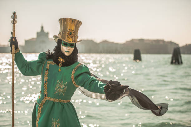Masked Person in Green Carnival Costume with Golden Hat Posing near Canale Grande, Venice stock photo