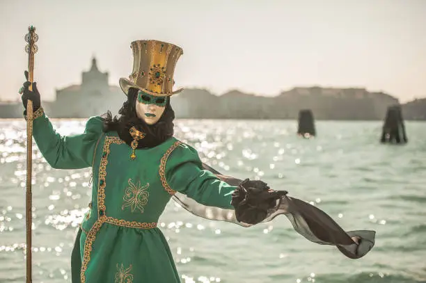 Masked Person in Green Carnival Costume with Golden Hat Posing near Canale Grande, Venice