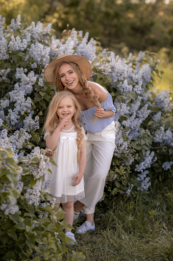 Young Beautiful Mom with Long Blonde Hair Walks in the Garden with Daughter.