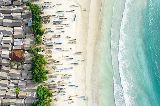 View from above, stunning aerial view of a fishing village with houses and boats on a white sand beach bathed by a beautiful turquoise sea. Tanjung Aan Beach, east of Kuta Lombok, West Nusa Tenggara, Indonesia.