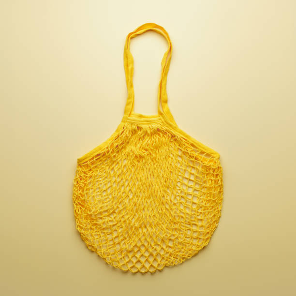Zero waste concept. Reusable mesh shopping bag for food products lies on yellow background. Vertical orientation, top view.