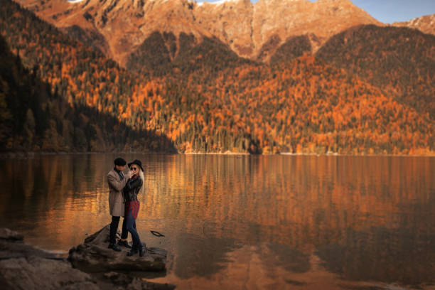 para kochanków mężczyzna i kobieta stoją w pobliżu jeziora między górami - sunrise beach couple hiking zdjęcia i obrazy z banku zdjęć