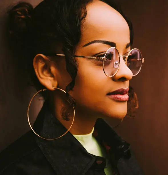 Side view close-up portrait of a beautiful young and confident African American woman with trendy accessories as round earrings and eyeglasses looking away while thinking of future plans