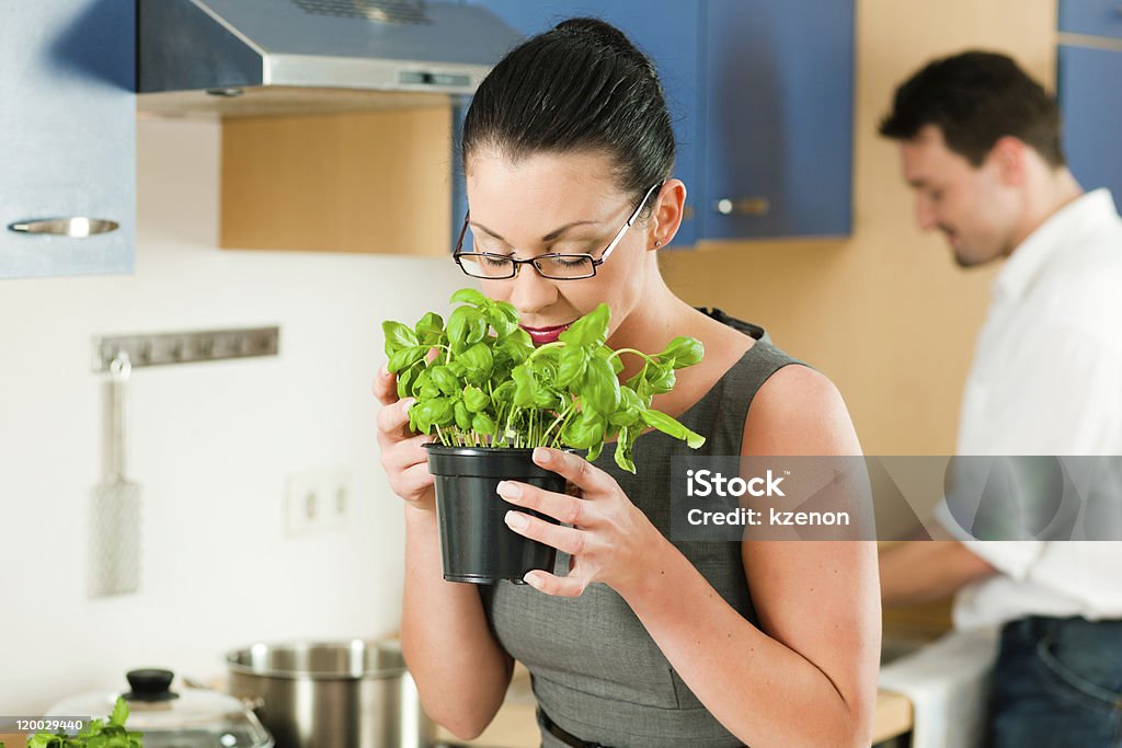Couple cooking together in kitchen Woman smells the aroma of a basil pot in her kitchen – in the background her husband is cooking 40-49 Years Stock Photo