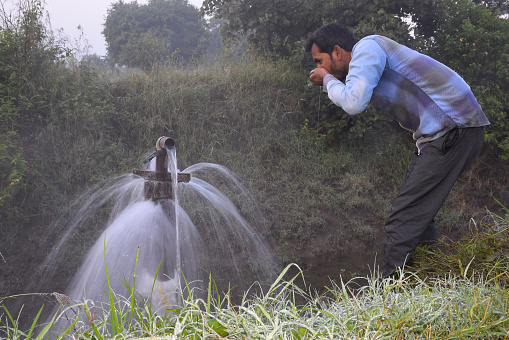 Agricultural equipment for field irrigation, an Indian farmer drinking water from water jet overflowing on his farm, Rain fog, selective focus