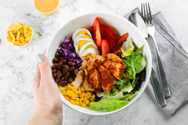 istock Healthy bowl in woman's hand. Lunch bowl with chicken, egg, tomatoes, lettuce, corn, red beans, red cabbage. Clean food and dieting nutrition concept. Top view, copy space, flat lay 1200318445