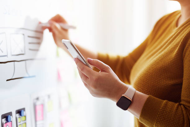 istock Woman with mobile phone and red marker planning website on whiteboard 1200338029