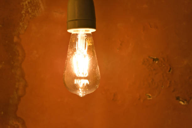 lampadina luminosa incandescente di fronte a una parete di cemento - victorian style flash foto e immagini stock