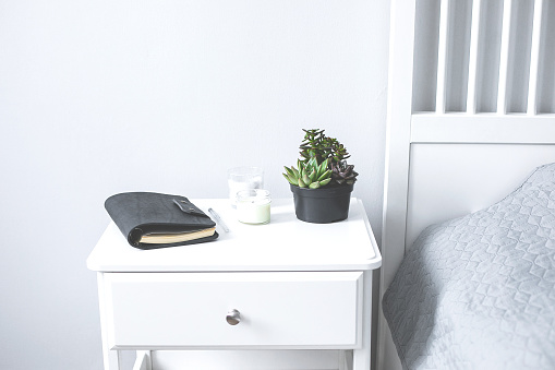 Tiny succulents, candles and black notebook on bedside table in the bedroom in scandinavian style home. Scandinavian interior in gray and white colors
