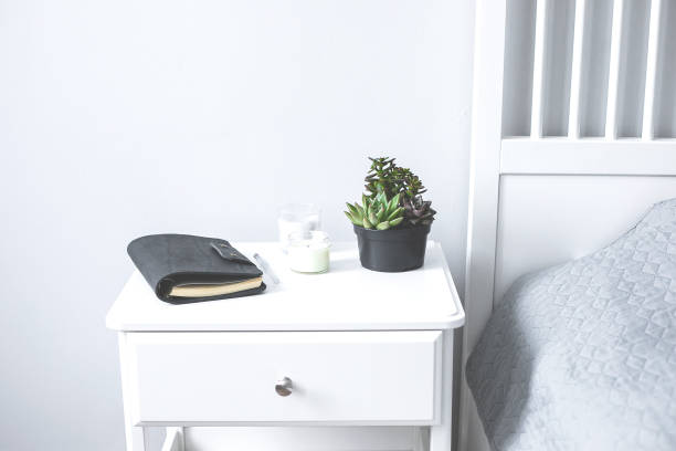 Tiny succulents, candles and black notebook on bedside table in the bedroom in scandinavian style home. Scandinavian interior in gray and white colors Tiny succulents, candles and black notebook on bedside table in the bedroom in scandinavian style home. Scandinavian interior in gray and white colors night table stock pictures, royalty-free photos & images