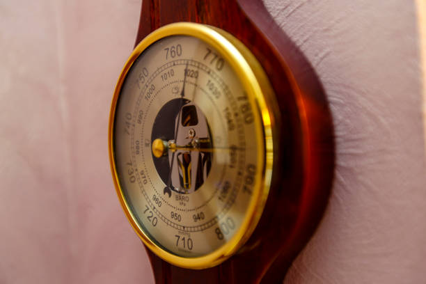 A vintage barometer Clock hangs on a pink wall. shot on a large aperture, blurry background. Golden rim, wooden base, beautiful arrows